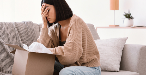 Dekorbild på besviken ung kvinna som sitter i soffa med öppnad kartong.